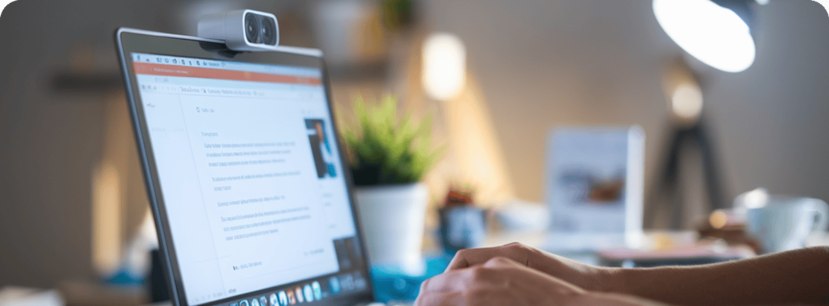Eine Person tippt auf einer Tastatur vor einem Computermonitor, auf dem ein Dokument angezeigt wird, möglicherweise um SEO-Texte schreiben zu lassen; über dem Bildschirm ist eine Webcam angebracht.