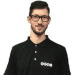 Ein Mann mit kurzen dunklen Haaren und Brille trägt ein schwarzes Poloshirt mit weißem „ALBI“-Schriftzug auf der Brust und steht vor einem dunklen Hintergrund.