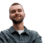 Ein junger Mann mit kurzen Haaren und Bart lächelt mit verschränkten Armen und trägt eine graue Jacke über einem weißen Hemd, isoliert auf einem transparenten Hintergrund.