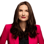 Frau mit langem braunem Haar, trägt einen leuchtend rosa Blazer und ein schwarzes Oberteil, blickt leicht nach oben und hat einen neutralen Gesichtsausdruck.