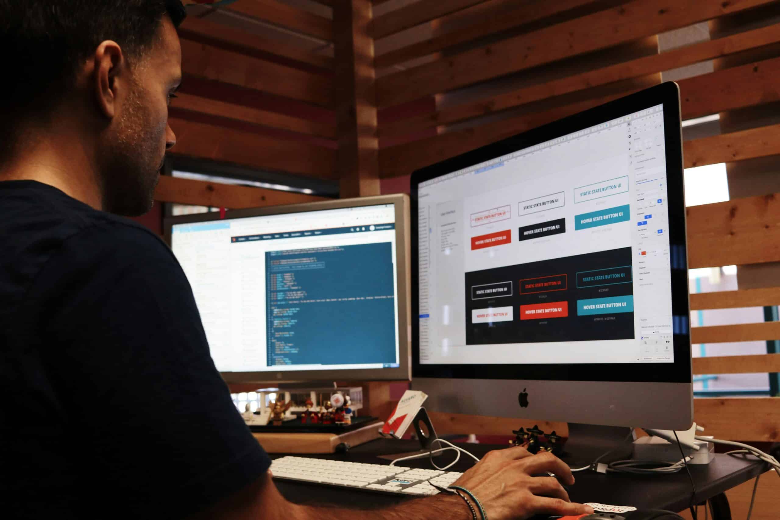 Eine Person, die an einem Schreibtisch mit zwei Monitoren arbeitet, von denen einer Code anzeigt und der andere ein Designmodell. Sie demonstriert, was ein Webdesigner macht, indem sie sowohl Entwicklungs- als auch kreative Designaufgaben in Einklang bringt.