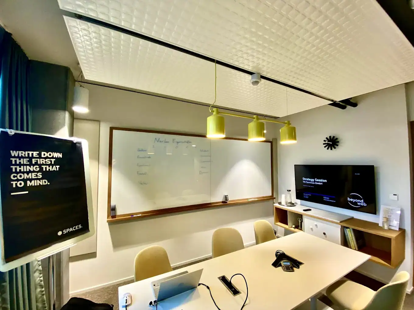 Ein moderner Konferenzraum mit einem langen Tisch, Stühlen, einem Whiteboard, einem Fernsehbildschirm mit der Aufschrift „Strategie-Sitzung“ und einem Schild mit der Aufschrift „Schreiben Sie das Erste auf, was Ihnen in den Sinn kommt.“.