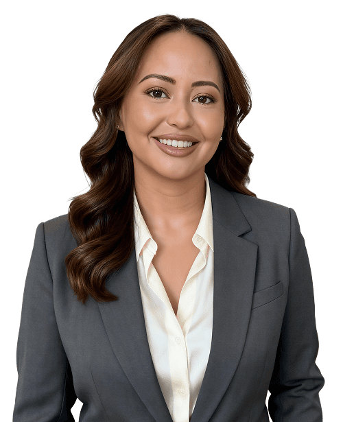 Eine Frau mit langen braunen Haaren, die einen grauen Blazer und eine weiße Bluse trägt, lächelt in die Kamera vor einem schlichten weißen Hintergrund.