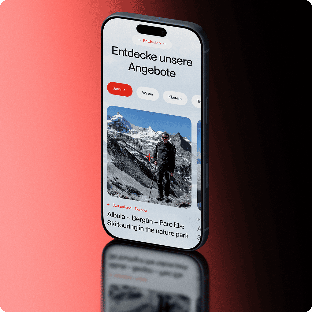 Ein Smartphone zeigt die deutschsprachige Reise-Website von Alpine Action Unlimited an, die einen Mann mit Wanderstöcken in einer verschneiten Berglandschaft und Optionen für saisonale Angebote zeigt.