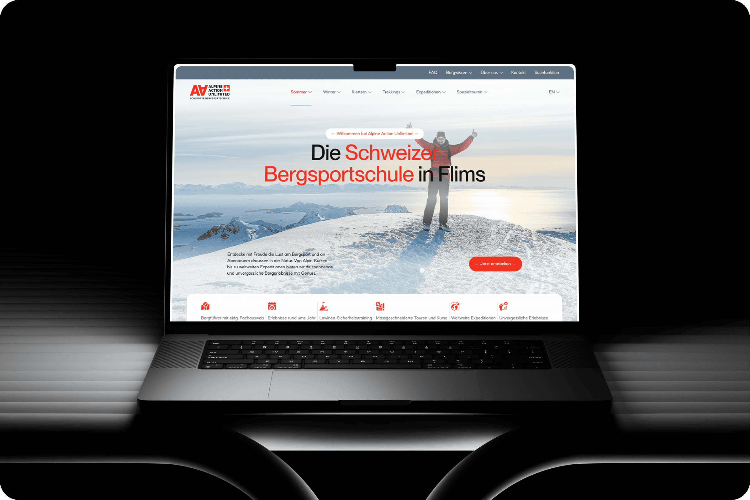 Ein Laptop zeigt die Website von Alpine Action Unlimited, einer Bergsportschule, mit einer Person, die auf einem verschneiten Gipfel steht, mit Bergen im Hintergrund und deutschem Text auf dem Bildschirm.