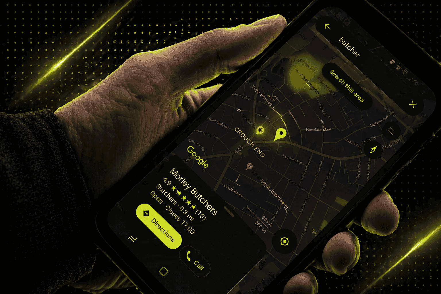 Eine Hand hält ein Smartphone, auf dem eine Karten-App mit einer Suche nach Metzgereien angezeigt wird; ein Ort wird auf der Karte markiert und ein Geschäftseintrag wird angezeigt.